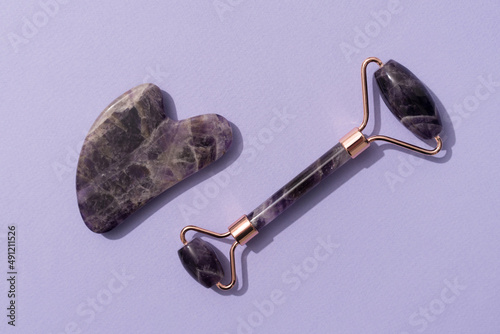 Facial massage kit - amethyst gua sha tool and face roller on trendy purple background. Face roller, massager made from natural stones. Skin care routine photo