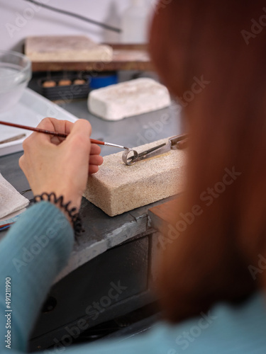 a woman working in her artisan jewelry workshop using a small brush on a ring to perform her work on a block of stone