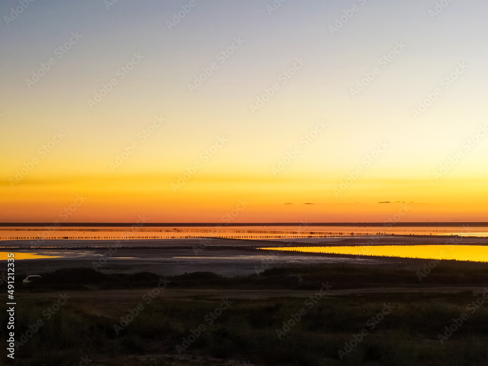 Twilight on the salt lake beach under the boundless sky. Calm evening view with mirror water at sunset.