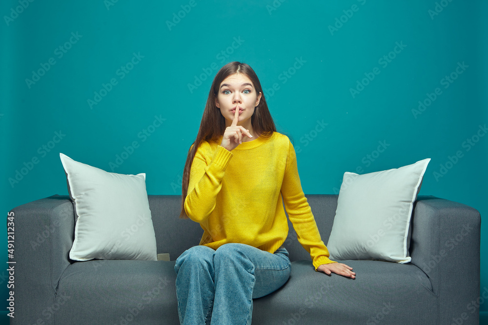 Funny young girl show silence gesture ask to be quiet, sitting on sofa, watching modern interesting movie or series Funny young girl show silence gesture ask to be quiet, sitting on sofa, watching modern interesting movie or series