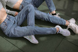 Cropped shot of two young girls in blue jeans and  sneakers laying on green playground in the sun.