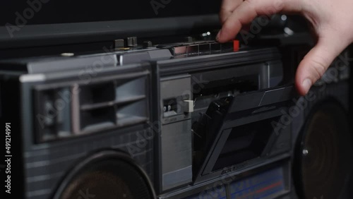 A man's hand inserts a cassette into a tape recorder and presses the play button
