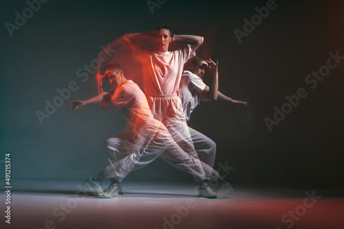 Fototapeta Naklejka Na Ścianę i Meble -  Dancing young sporty girl moving in fiery hip-hop dance in red neon studio light. Long exposure. Breakdancing school ad