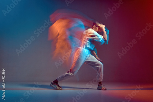 Fototapeta Naklejka Na Ścianę i Meble -  Sportive girl with short hair dancing hip-hop in stylish sportswear in colorful neon light at dance hall. Long exposure