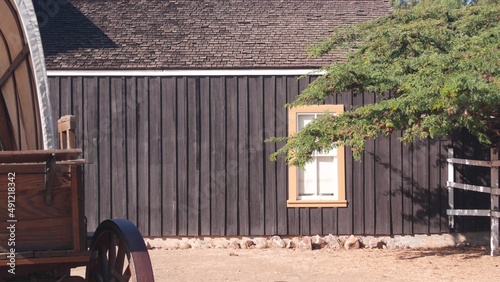 Old wooden retro covered wagon on wheels, wild west pioneer ranch. Western historic retro cart, traditional vintage transport. Rural house wall, building exterior. Countryside farm or cowboy saloon. photo