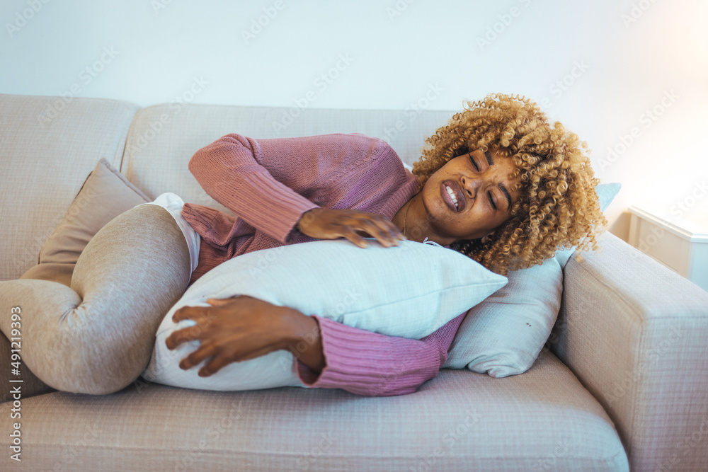 Cropped shot of an attractive young woman lying down on her bed and suffering from period pains at home. Shot of a young woman experiencing stomach pain on the sofa at home