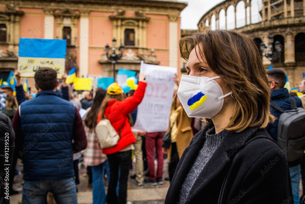 Ukrainian Woman with Determined Look Wearing Blue and Yellow Painted Mask in Demonstration in Favor of Ukraine and Peace With Protersters Behind