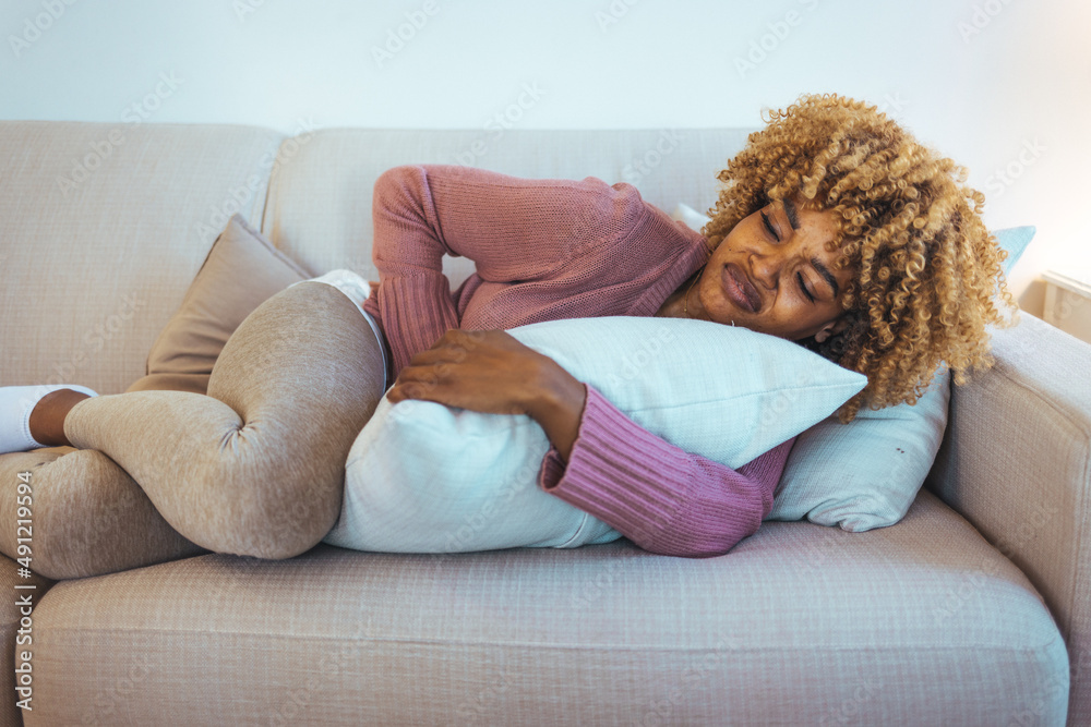 Woman feeling pain to the stomach lying on sofa. Cropped shot of a woman suffering from stomach cramps on the sofa at home. Ouch! My tummy. Woman feeling pain to the stomach lying on sofa. Cropped shot of a woman suffering from stomach cramps on the sofa at home. Ouch! My tummy.