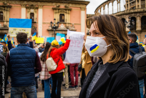 Ukrainian Woman with Determined Look Wearing Blue and Yellow Painted Mask in Demonstration in Favor of Ukraine and Peace With Protersters Behind photo
