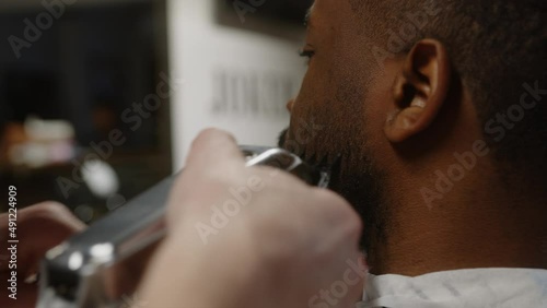 Fashionable dark-skinned guy gets a beautiful beard hairstyle in a barbershop