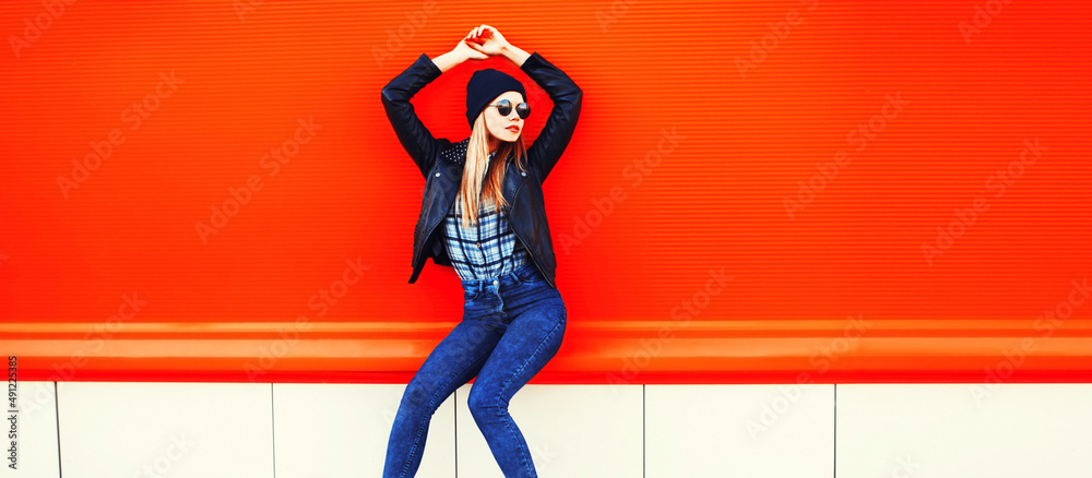 Obraz premium Portrait of stylish blonde young woman in black rock style on vivid background