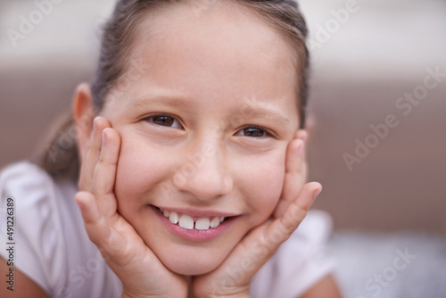Childhood purity. A young girl with her hands on her face smiling at the camera - close-up.