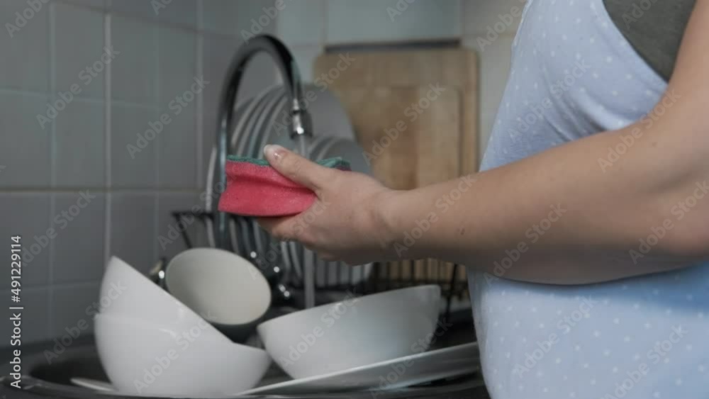 Close up of Hands of Female Washing Dishes with Detergent, Pouring Dish Soap on a Sponge in Kitchen. Slow Motion. Selective Focus. Domestic Housework and Housekeeping Concept Close up of Hands of Female Washing Dishes with Detergent, Pouring Dish Soap on a Sponge in Kitchen. Slow Motion. Selective Focus. Domestic Housework and Housekeeping Concept
