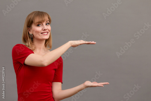 Young beautiful blonde woman wearing stylish red dress making frame with her hands on a gray wall background. Copy, empty space for text