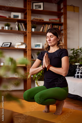 A middle-aged woman prays and practices yoga at home.