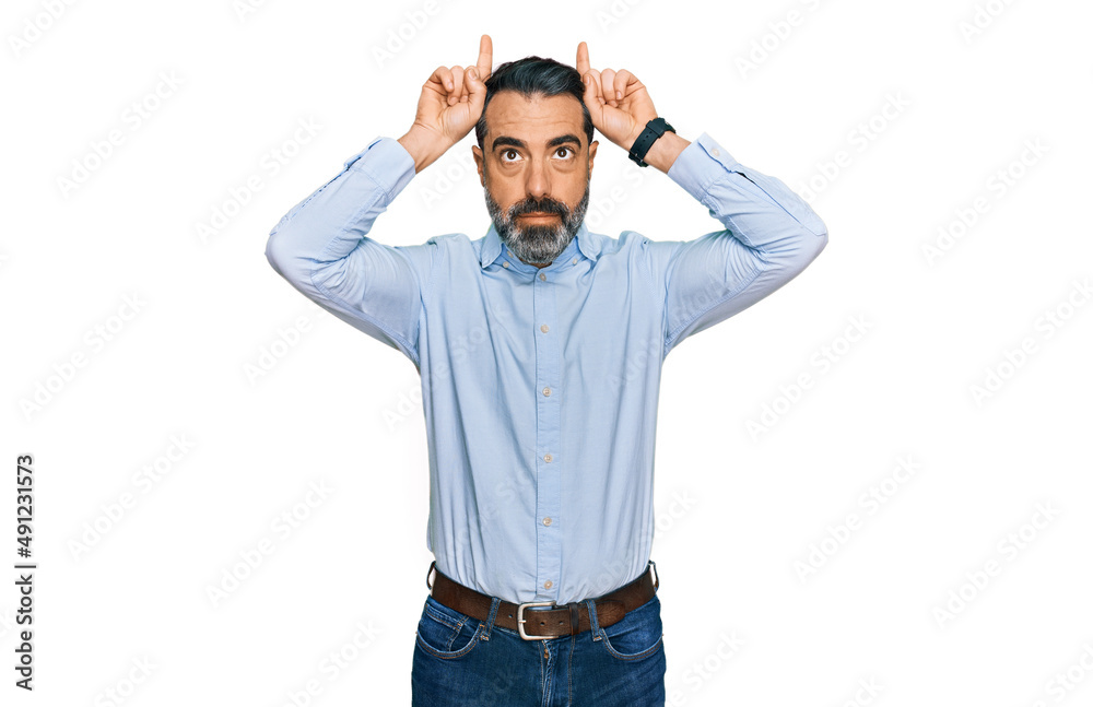 Fototapeta premium Middle aged man with beard wearing business shirt doing funny gesture with finger over head as bull horns