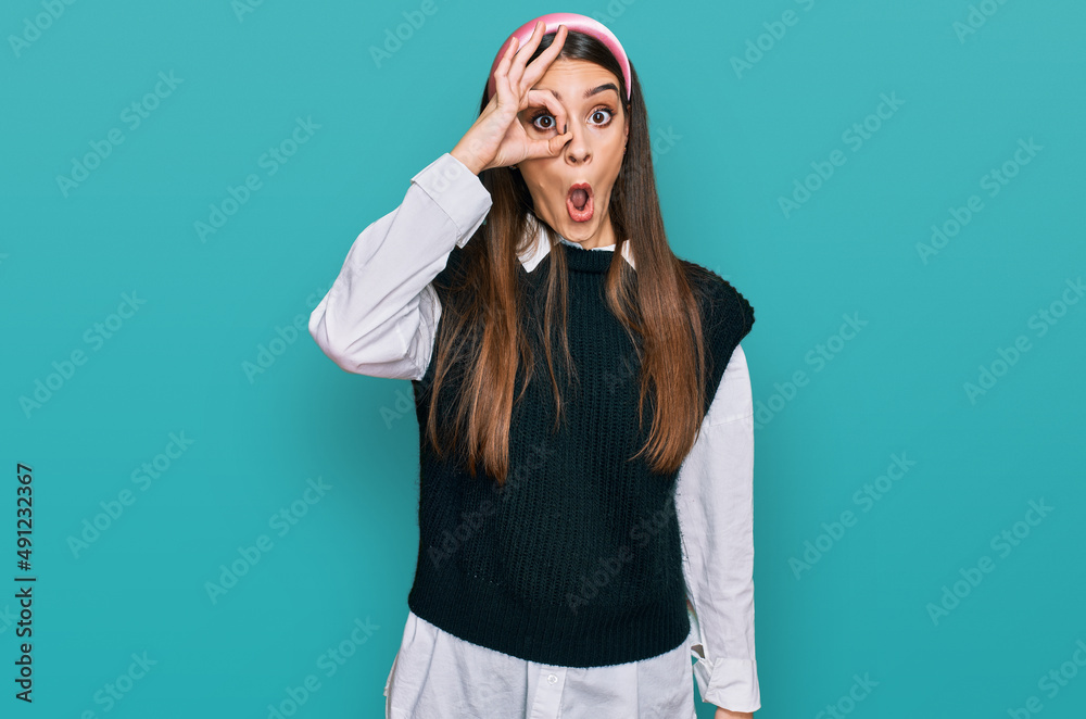 Young beautiful woman wearing casual white shirt doing ok gesture shocked with surprised face, eye looking through fingers. unbelieving expression. Young beautiful woman wearing casual white shirt doing ok gesture shocked with surprised face, eye looking through fingers. unbelieving expression.