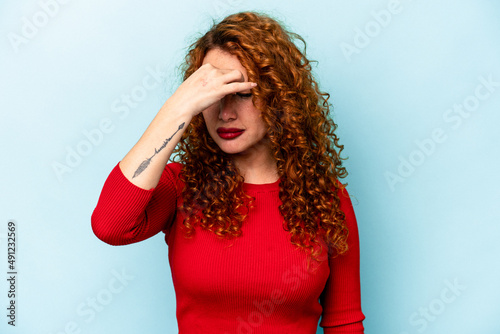 Young ginger caucasian woman isolated on blue background having a head ache, touching front of the face.