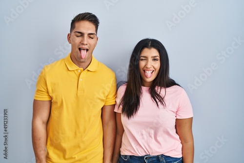 Young couple standing over isolated background sticking tongue out happy with funny expression. emotion concept.