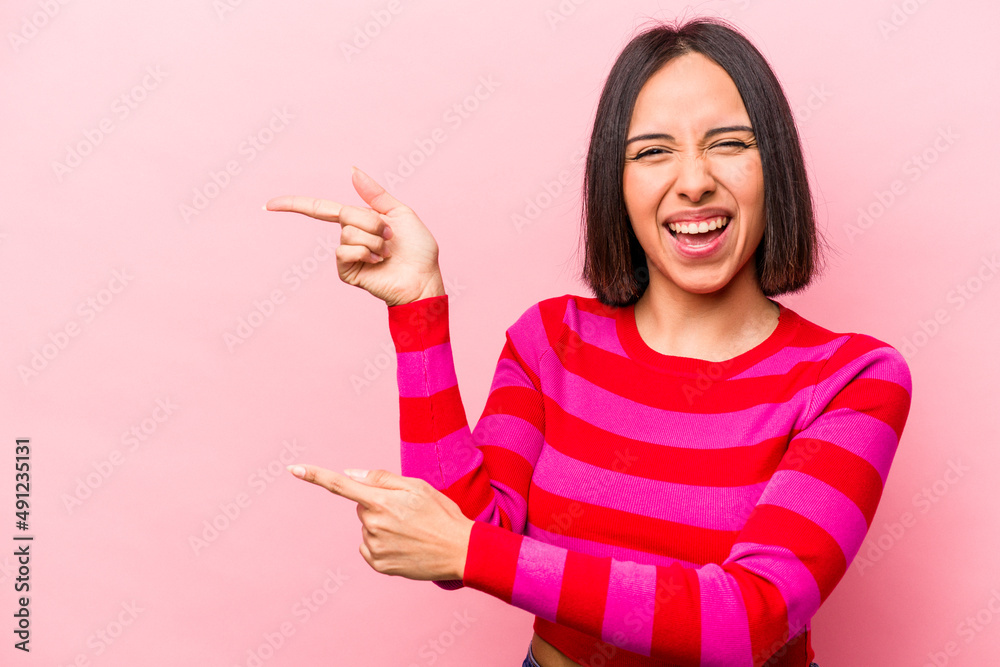 Young hispanic woman isolated on pink background pointing with forefingers to a copy space, expressing excitement and desire. Young hispanic woman isolated on pink background pointing with forefingers to a copy space, expressing excitement and desire.