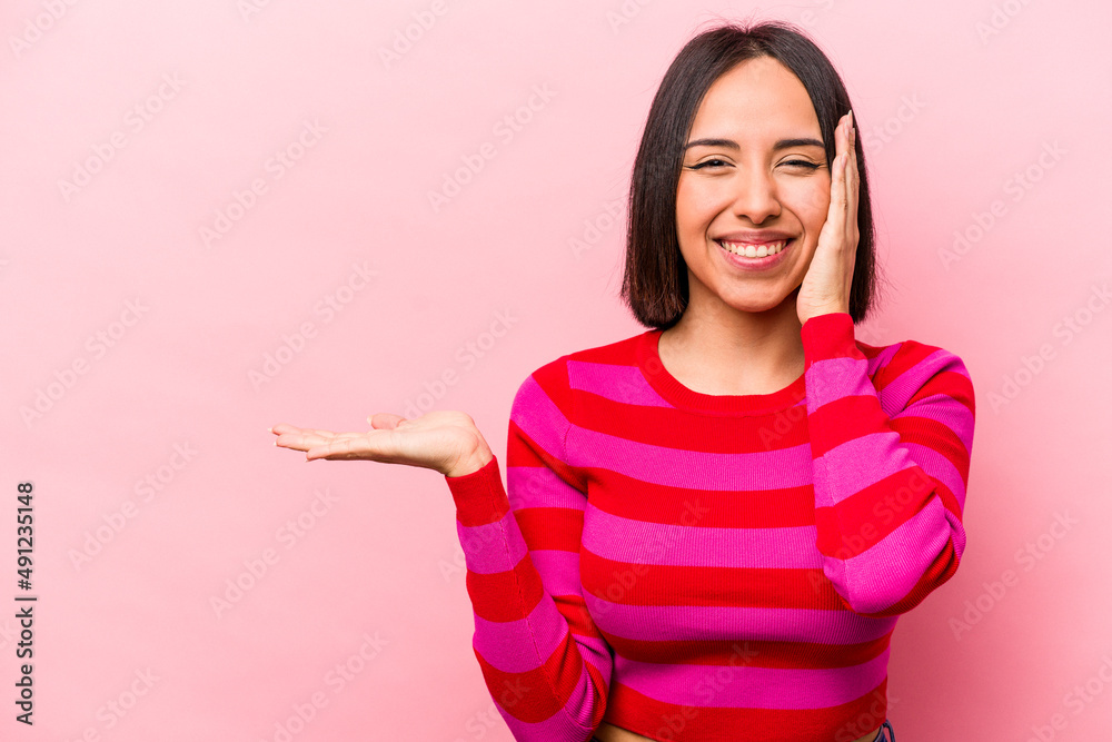 Young hispanic woman isolated on pink background holds copy space on a palm, keep hand over cheek. Amazed and delighted. Young hispanic woman isolated on pink background holds copy space on a palm, keep hand over cheek. Amazed and delighted.
