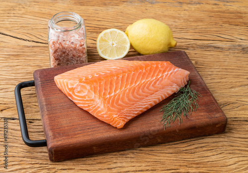 Raw salmon fillet with seasonings over wooden board