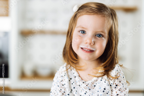 Close up of happy girl having yogurt mustache at home and looking at camera