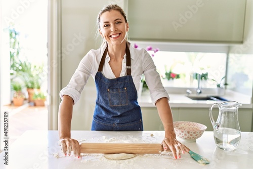 Young blonde woman smiling confident kneading pizza dough at kitchen