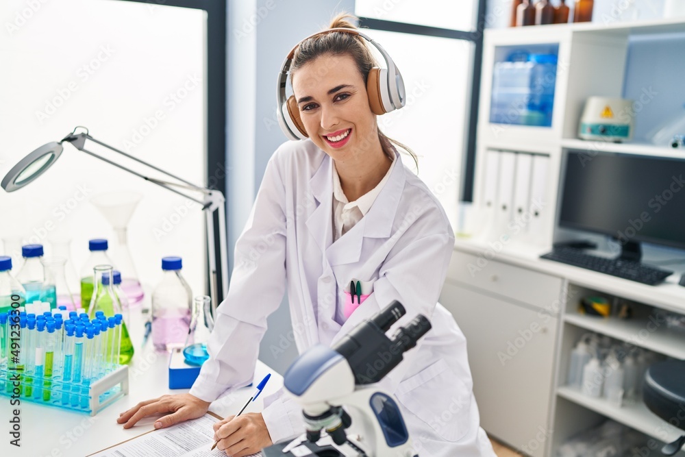 Young woman wearing scientist uniform listening to music writing report at laboratory