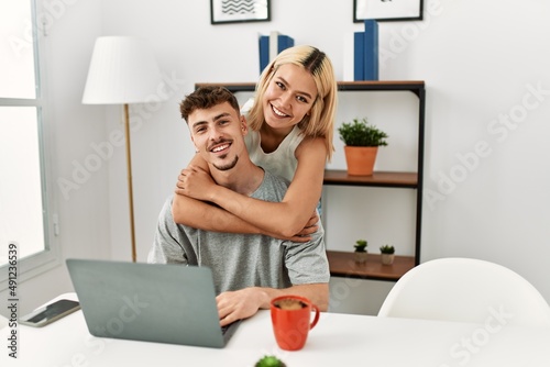 Young caucasian couple hugging and using laptop sitting on the desk at home.