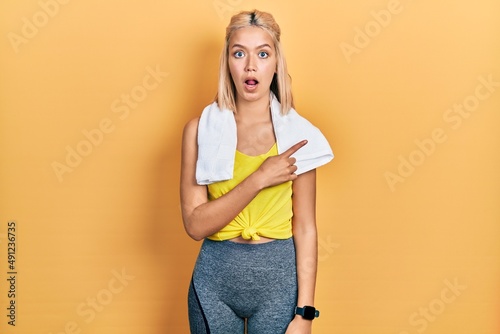 Beautiful blonde sports woman wearing workout outfit surprised pointing with finger to the side  open mouth amazed expression.