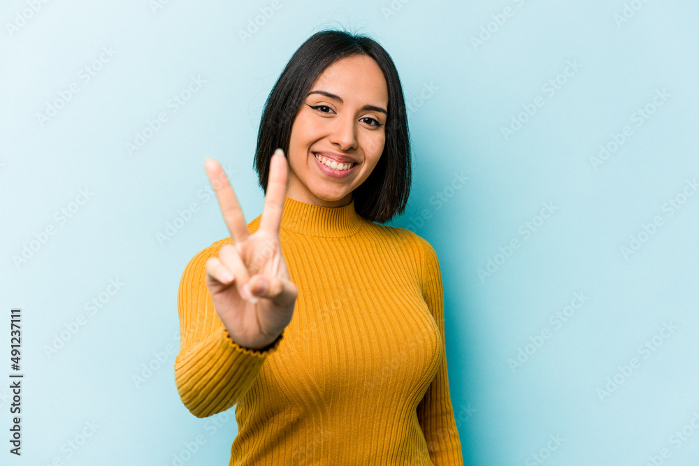 Young hispanic woman isolated on blue background joyful and carefree showing a peace symbol with fingers. Young hispanic woman isolated on blue background joyful and carefree showing a peace symbol with fingers.