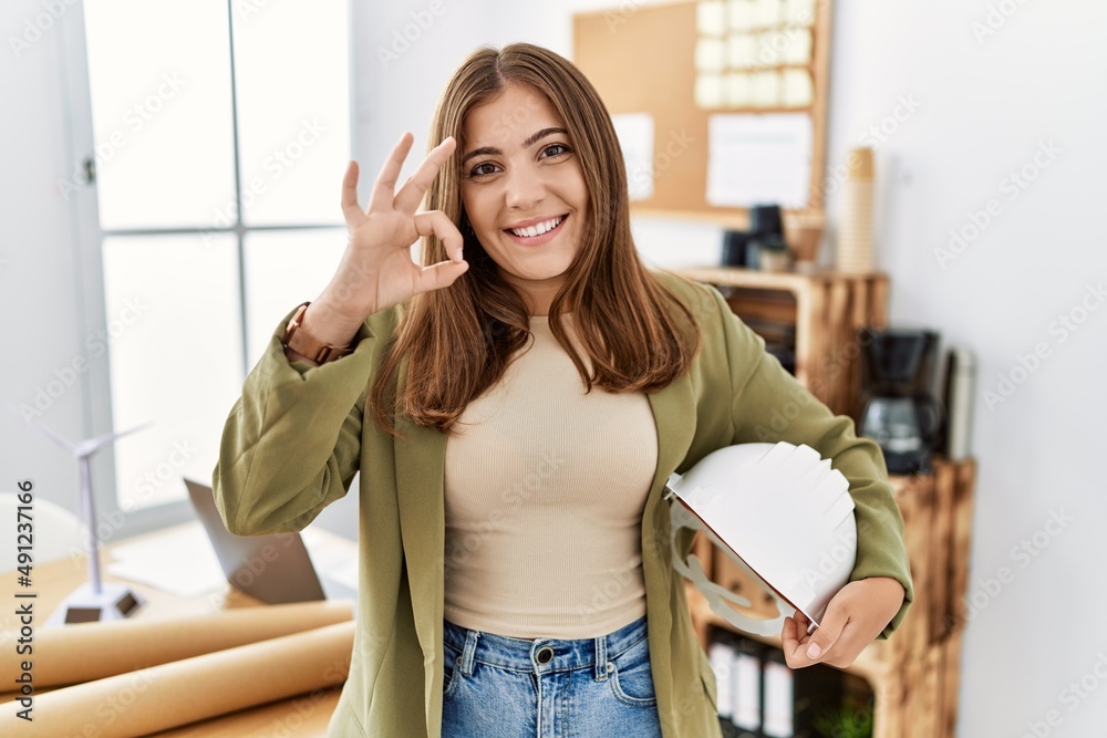 Young brunette woman holding architect hardhat at the office doing ok sign with fingers, smiling friendly gesturing excellent symbol Young brunette woman holding architect hardhat at the office doing ok sign with fingers, smiling friendly gesturing excellent symbol