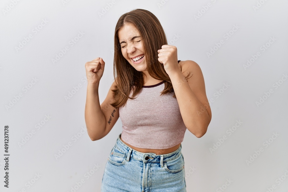 Young brunette woman standing over isolated background very happy and excited doing winner gesture with arms raised, smiling and screaming for success. celebration concept. Young brunette woman standing over isolated background very happy and excited doing winner gesture with arms raised, smiling and screaming for success. celebration concept.