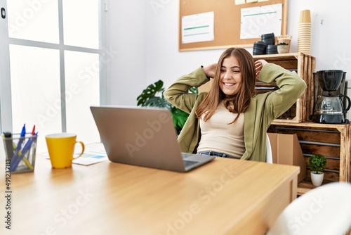 Young hispanic woman smiling confident relaxed with hands on head at office