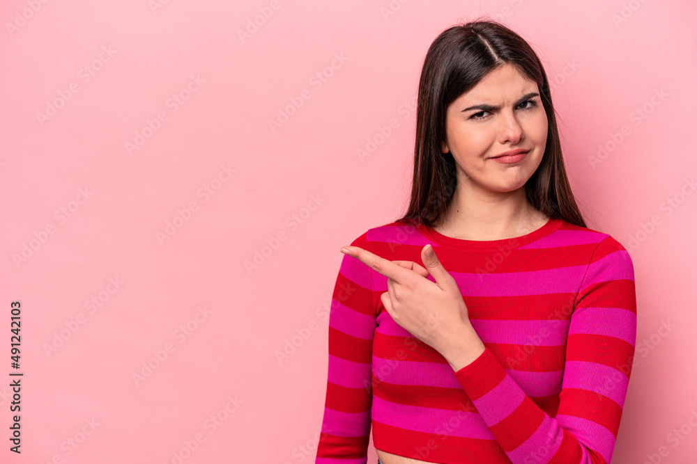 Young caucasian woman isolated on pink background smiling and pointing aside, showing something at blank space. Young caucasian woman isolated on pink background smiling and pointing aside, showing something at blank space.