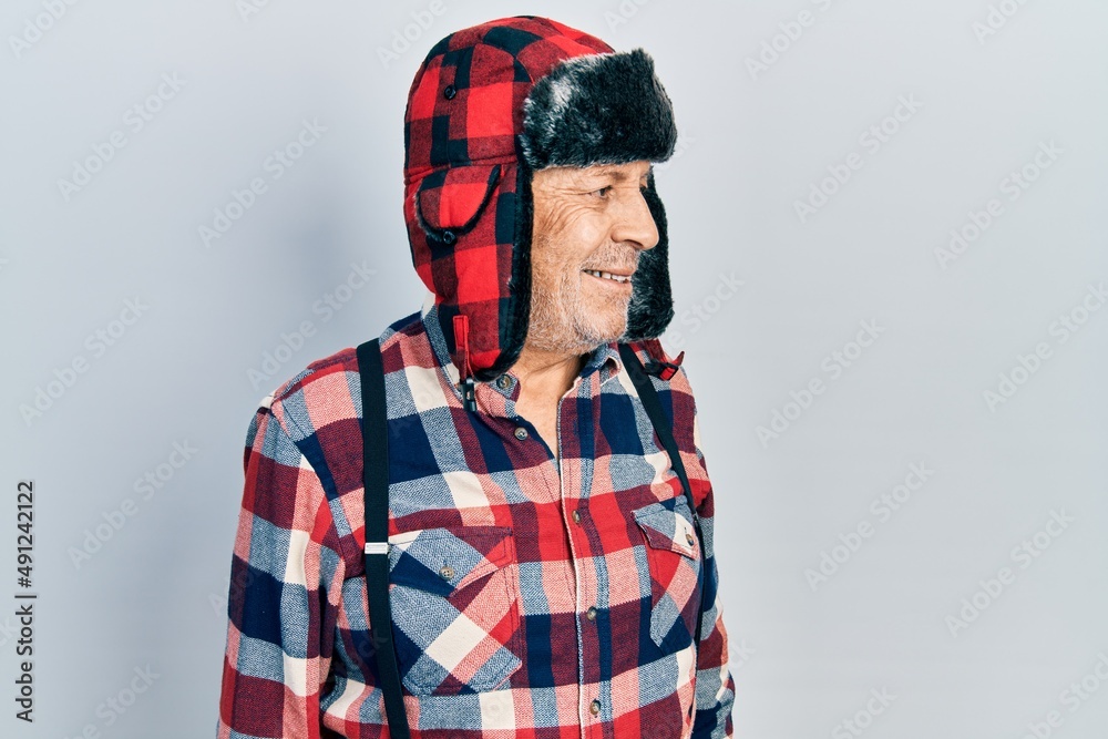 Handsome mature man wearing winter hat with ear flaps looking away to side with smile on face, natural expression. laughing confident. Handsome mature man wearing winter hat with ear flaps looking away to side with smile on face, natural expression. laughing confident.