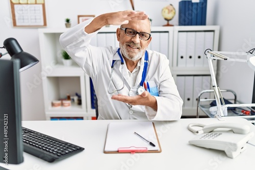 Mature doctor man at the clinic gesturing with hands showing big and large size sign  measure symbol. smiling looking at the camera. measuring concept.