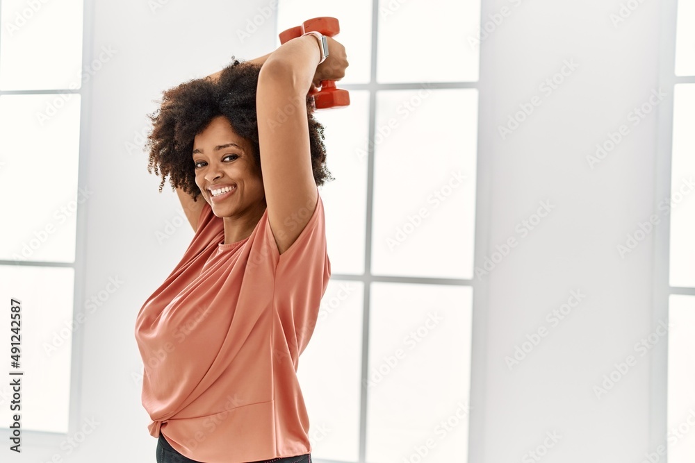 Young african american woman smiling confident training using dumbbells at sport center Young african american woman smiling confident training using dumbbells at sport center
