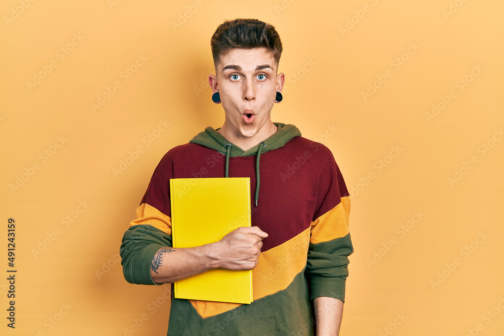 Young caucasian boy with ears dilation holding book scared and amazed with open mouth for surprise, disbelief face Young caucasian boy with ears dilation holding book scared and amazed with open mouth for surprise, disbelief face