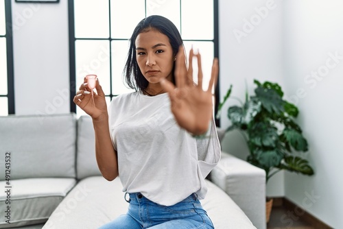 Young hispanic woman holding menstrual cup with open hand doing stop sign with serious and confident expression, defense gesture