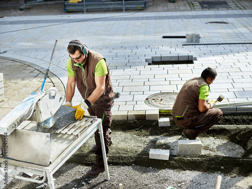 Paver cutting paving stone by coworker working in background photo