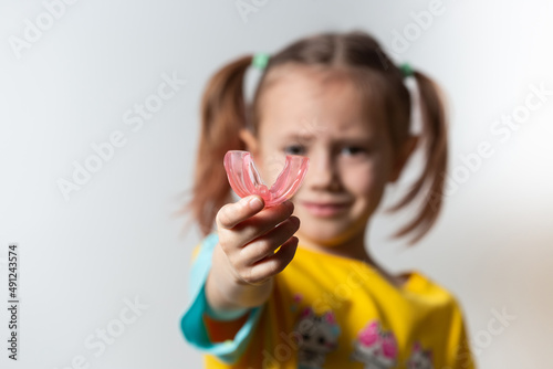 Cute little girl with blond hair is holding a pink dental myofunctional trainer