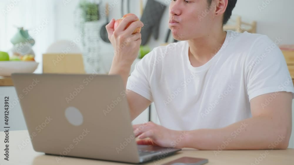 Asian business man eating healthy apple fruit while working from home.