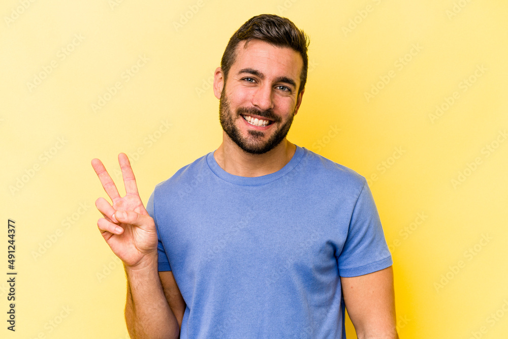 Young caucasian man isolated on yellow background showing victory sign and smiling broadly. Young caucasian man isolated on yellow background showing victory sign and smiling broadly.