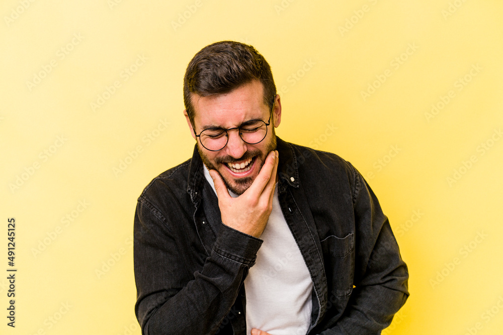 Young caucasian man isolated on yellow background laughs happily and has fun keeping hands on stomach. Young caucasian man isolated on yellow background laughs happily and has fun keeping hands on stomach.
