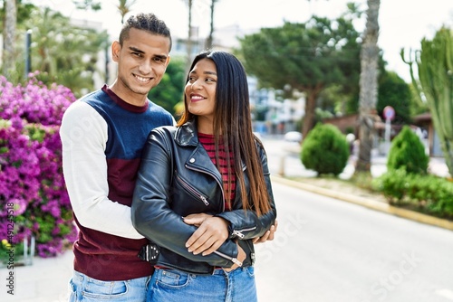 Young latin couple smiling happy and hugging walking at the street of city.