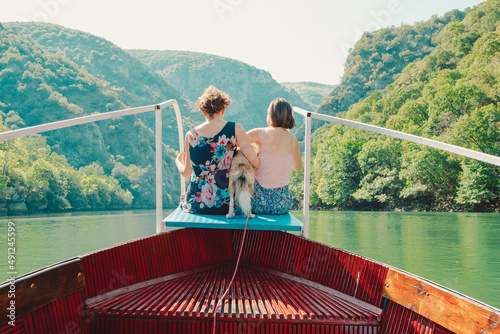 two friends hugging a dog on a boat in lake and green mountain area