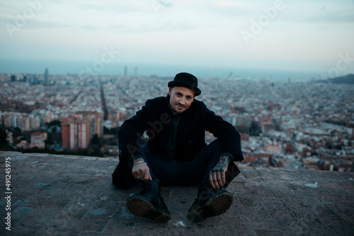 Man wearing black jacket sitting on terrace in front of city photo