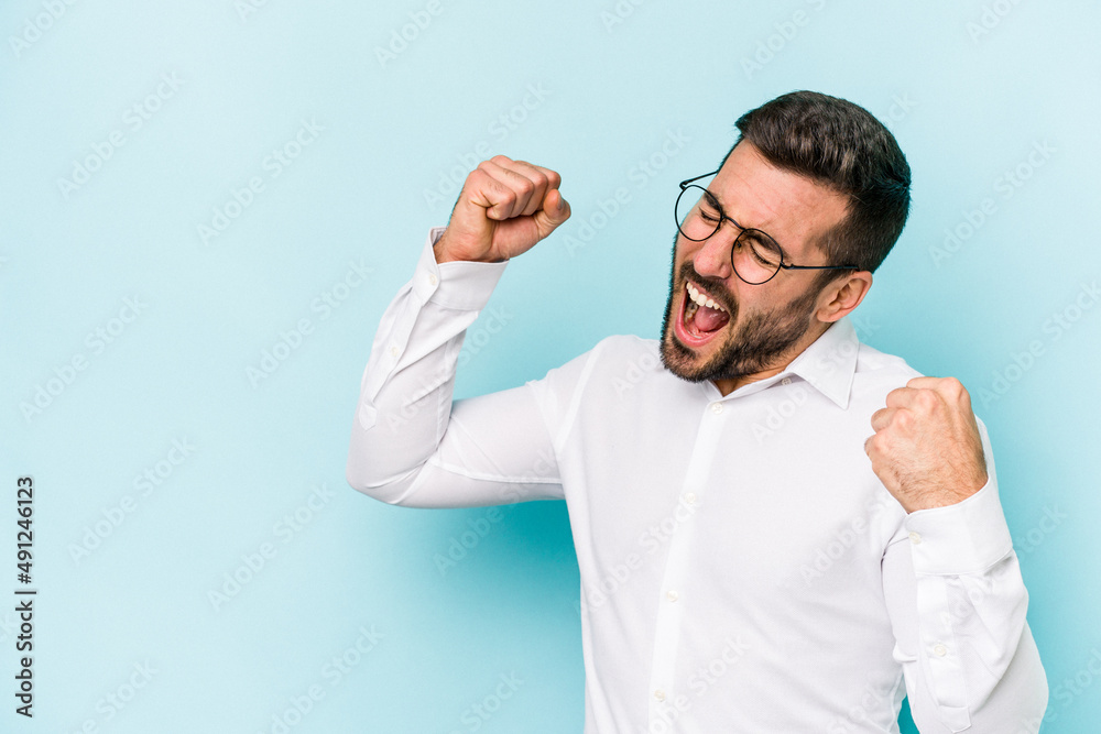 Young caucasian man isolated on blue background raising fist after a victory, winner concept. Young caucasian man isolated on blue background raising fist after a victory, winner concept.
